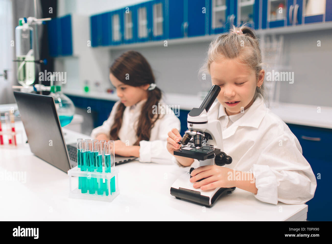Two little kids in lab coat learning chemistry in school laboratory