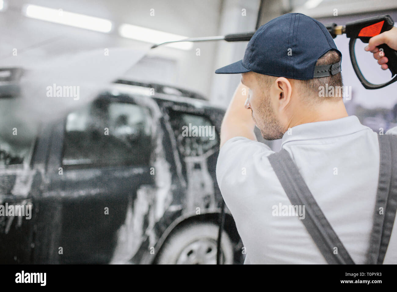 Worker in grey uniform stand at black car covered with foam. He holds