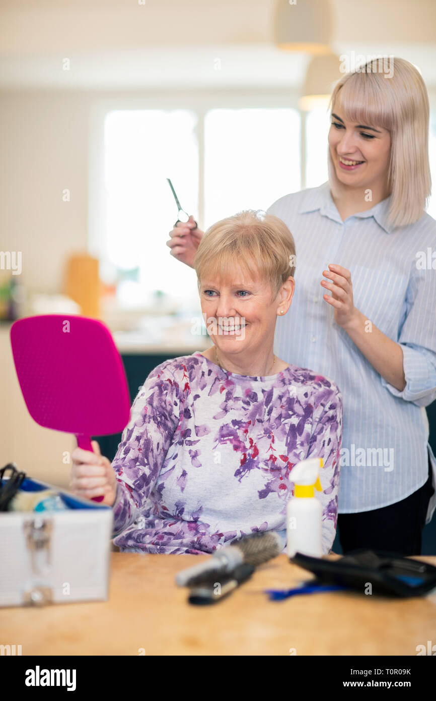 Female Mobile Hairdresser Cutting Senior Womans Hair At Home Stock Photo