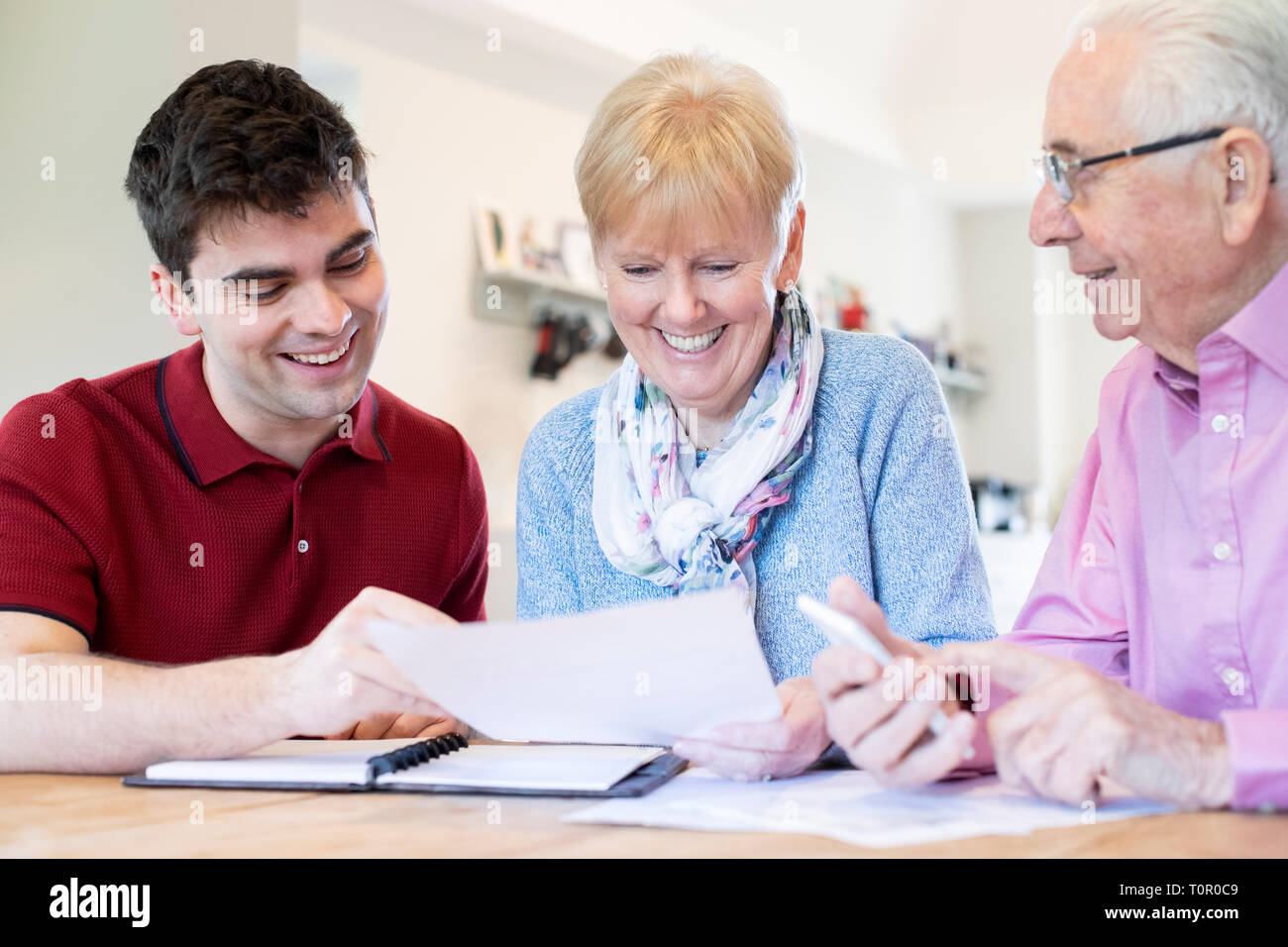 Young Man Helping Senior Couple With Financial Paperwork At Home Stock Photo