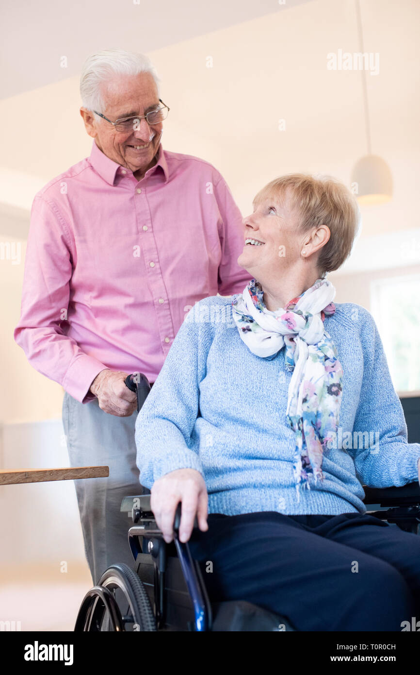 Senior Man Pushing Wife In Wheelchair At Home Stock Photo