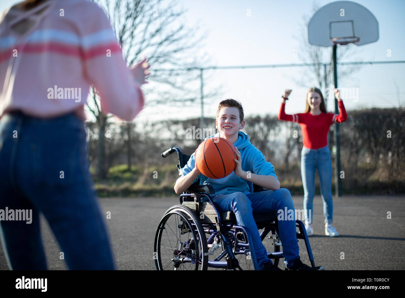 Teenage Boy In Wheelchair Playing Basketball With Friends Stock Photo
