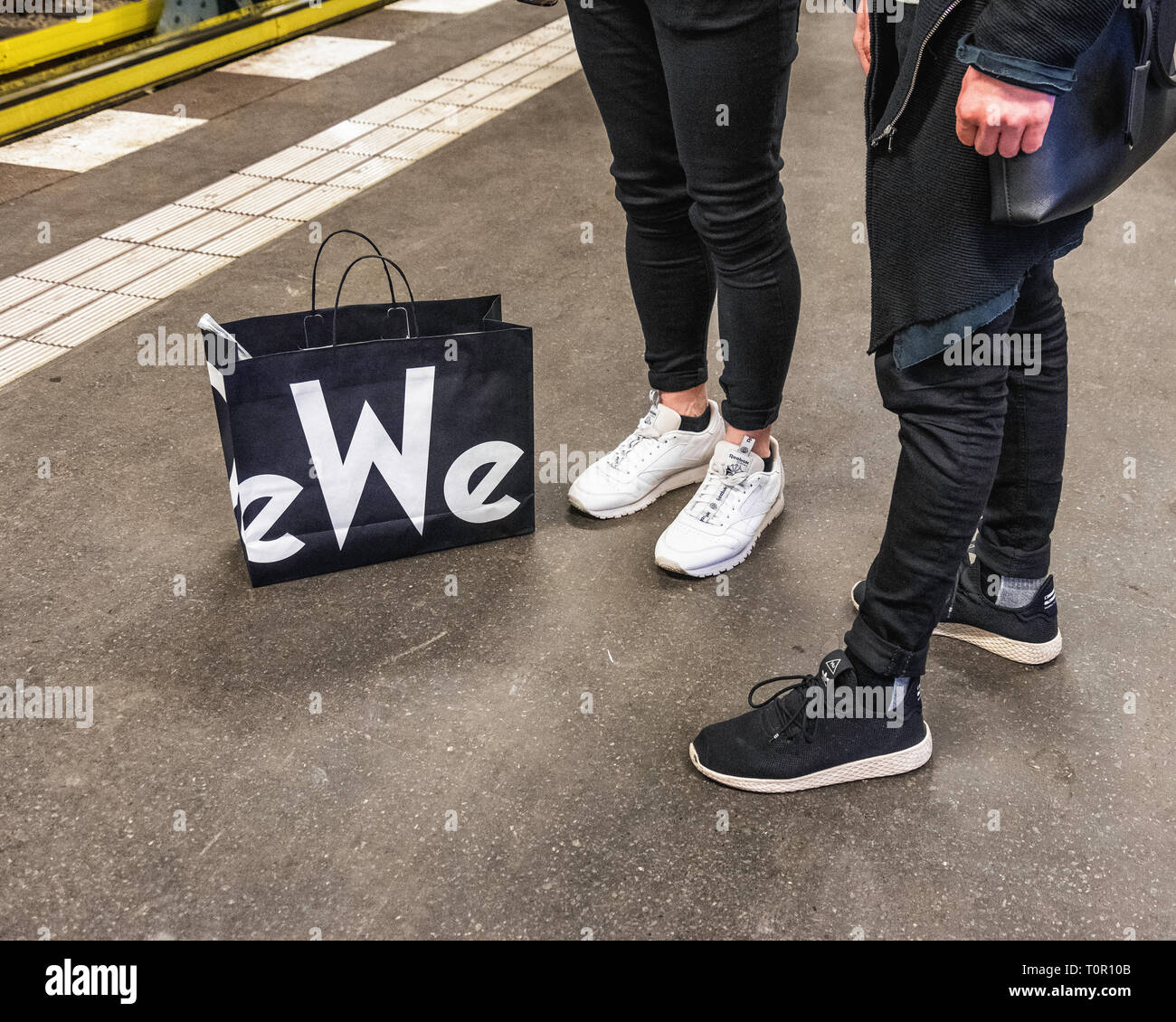 Two trendy young men with KaDeWe shopping bag waiting on Platform for train. Colour co-ordinated Stock Photo
