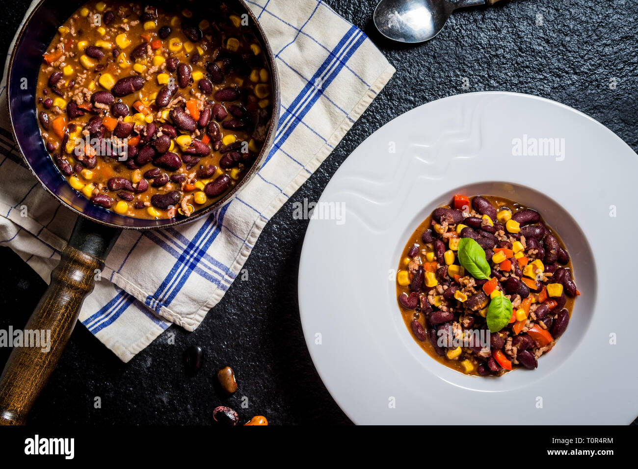 Chili or chilli corn carne. Cooked kidney bean, minced meat, chili, corn and pepper in white bowl  on black stone  table Stock Photo