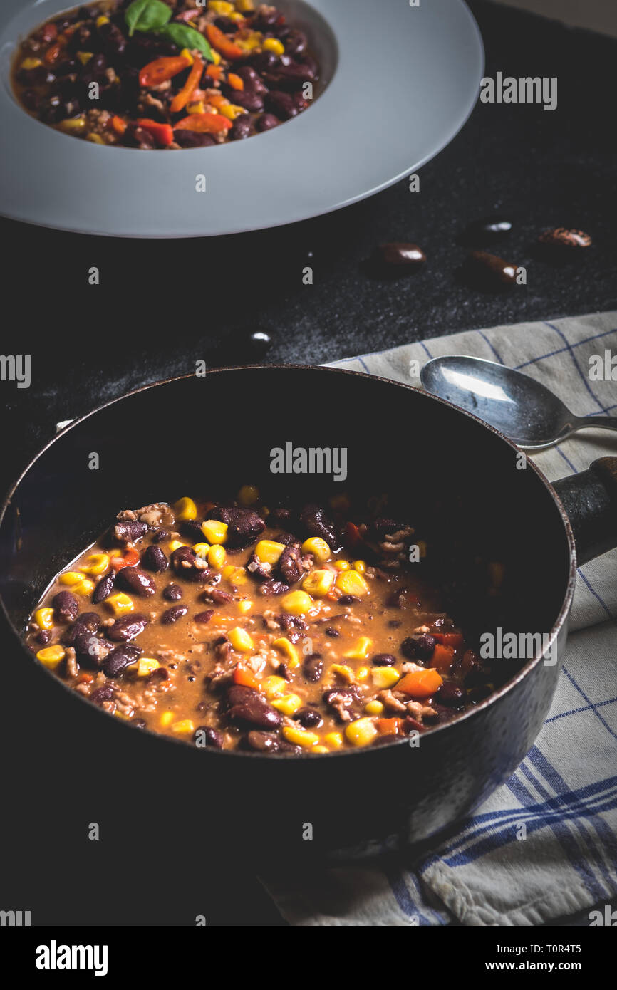 Chili or chilli corn carne. Cooked kidney bean, minced meat, chili, corn and pepper in white bowl  on black stone  table Stock Photo