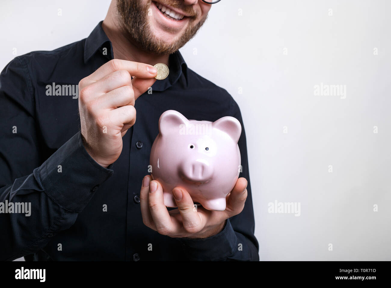 Young man putting coins in piggy bank. Saving for a rainy day Stock Photo