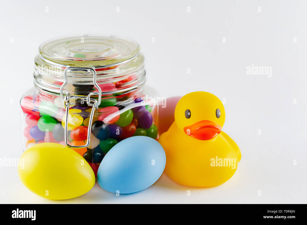 Rubber duck with colorful dyed easter eggs and a jar of jelly beans.  White background.  Copy space above. Stock Photo