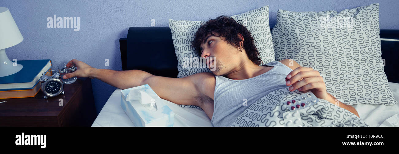 Young sick man taking medicines lying on bed Stock Photo