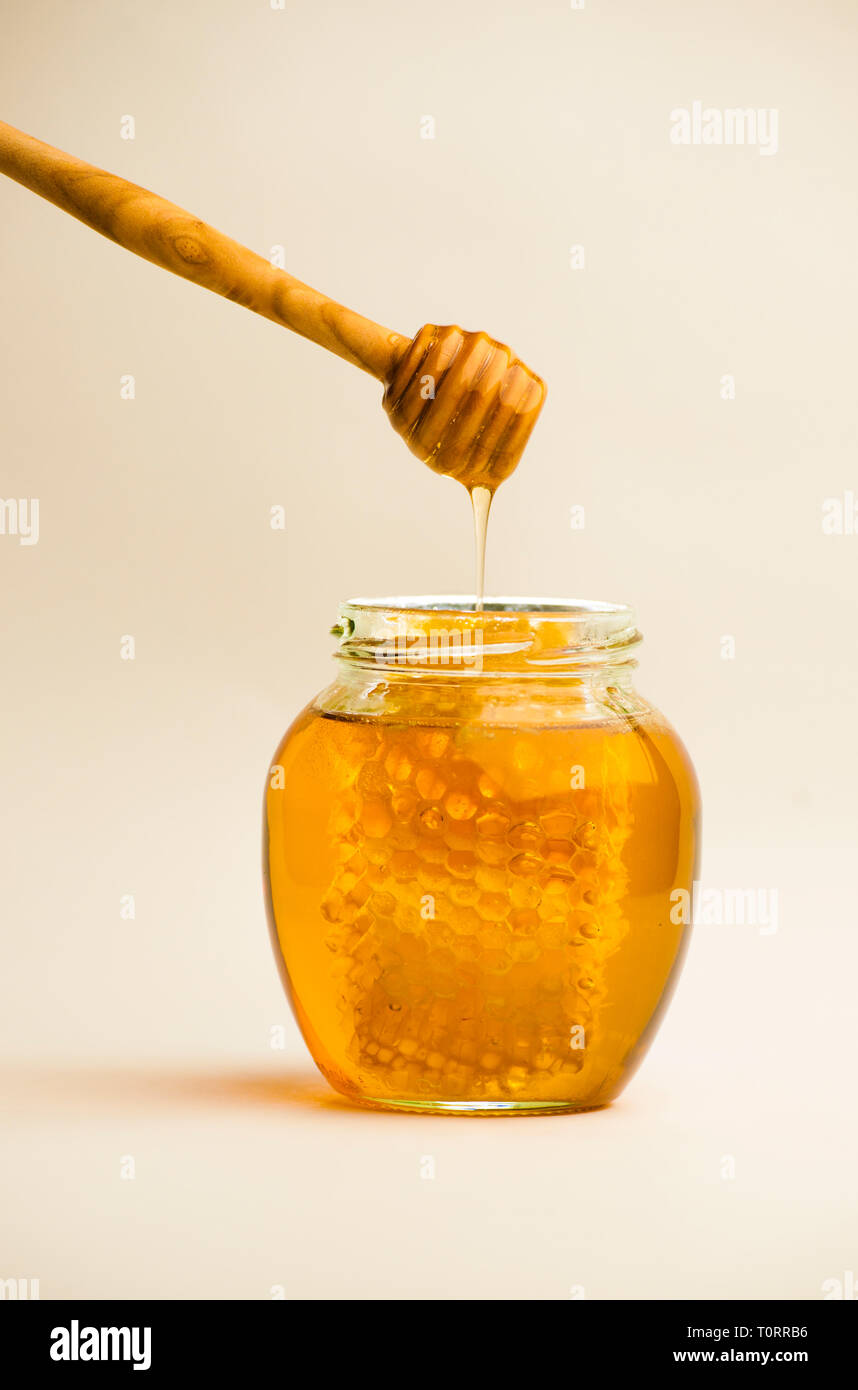 Honey Jar with Honeycomb and Wooden Dipper against a Plain Background Stock Photo