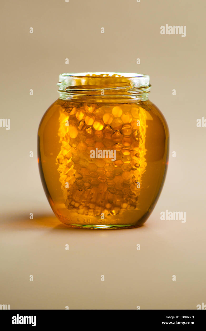 Honey Jar with Honeycomb and Wooden Dipper against a Plain Background Stock Photo