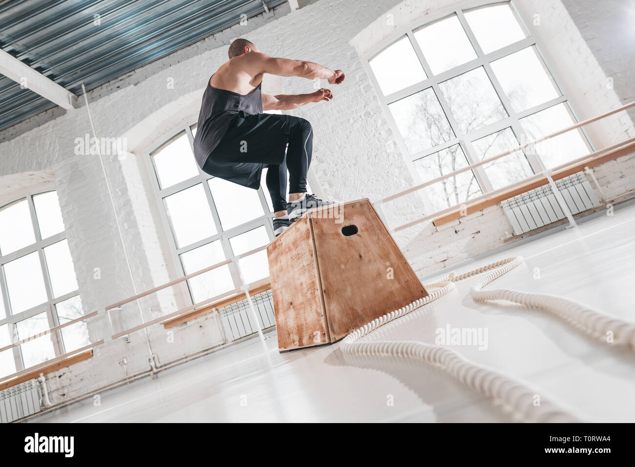 Fit male athlete doing box jump exercise in light hall. Sport man wearing in sportswear is