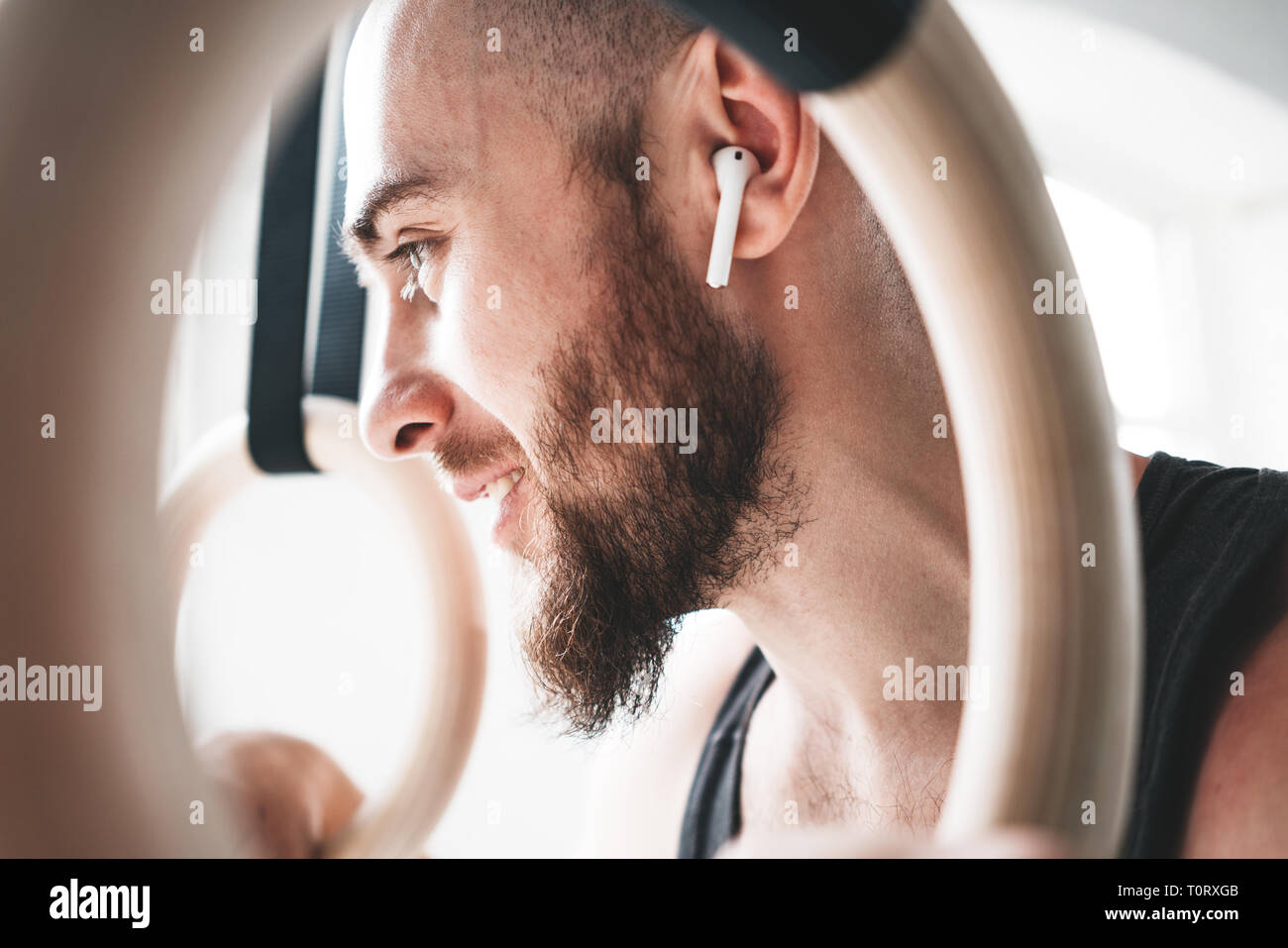 Close up view through gymnastics rings on bearded male athlete wearing