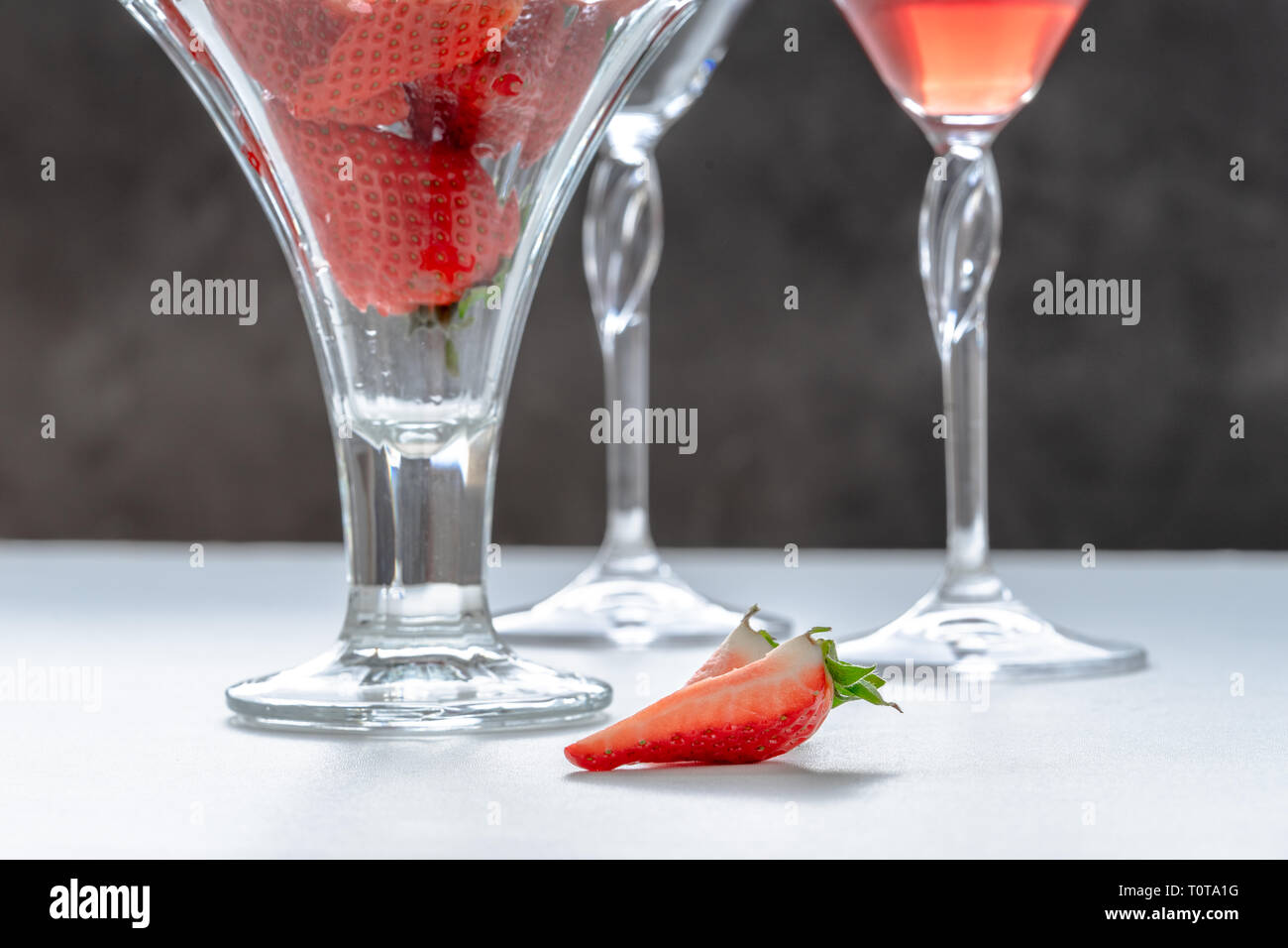 Two slices of strawberries on the table, glass with strawberries and a couple of glasses with drink Stock Photo