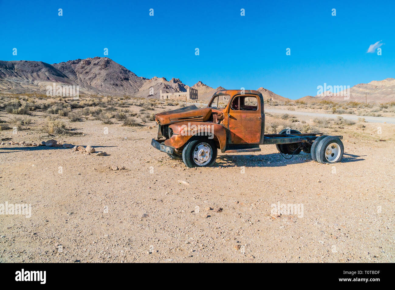 An abandoned wrecked old red truck in the foreground and the ruins of a