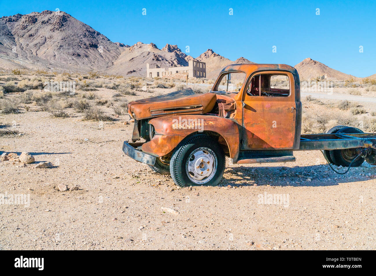 An abandoned wrecked old red truck in the foreground and the ruins of a