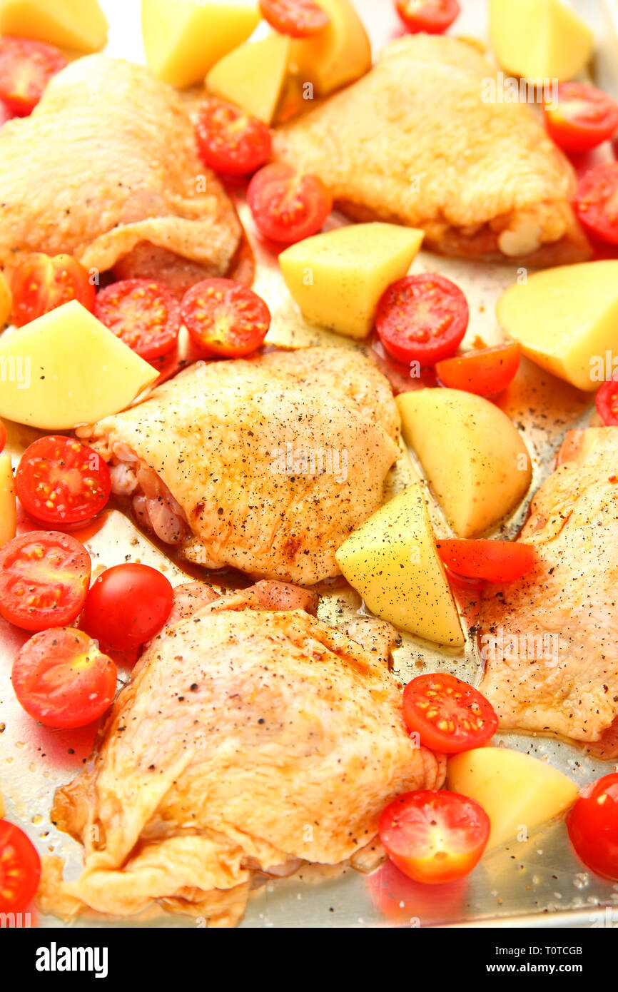 Seasoned chicken pieces with Yukon gold potatoes and cherry tomatoes on a sheet pan, vertical view Stock Photo