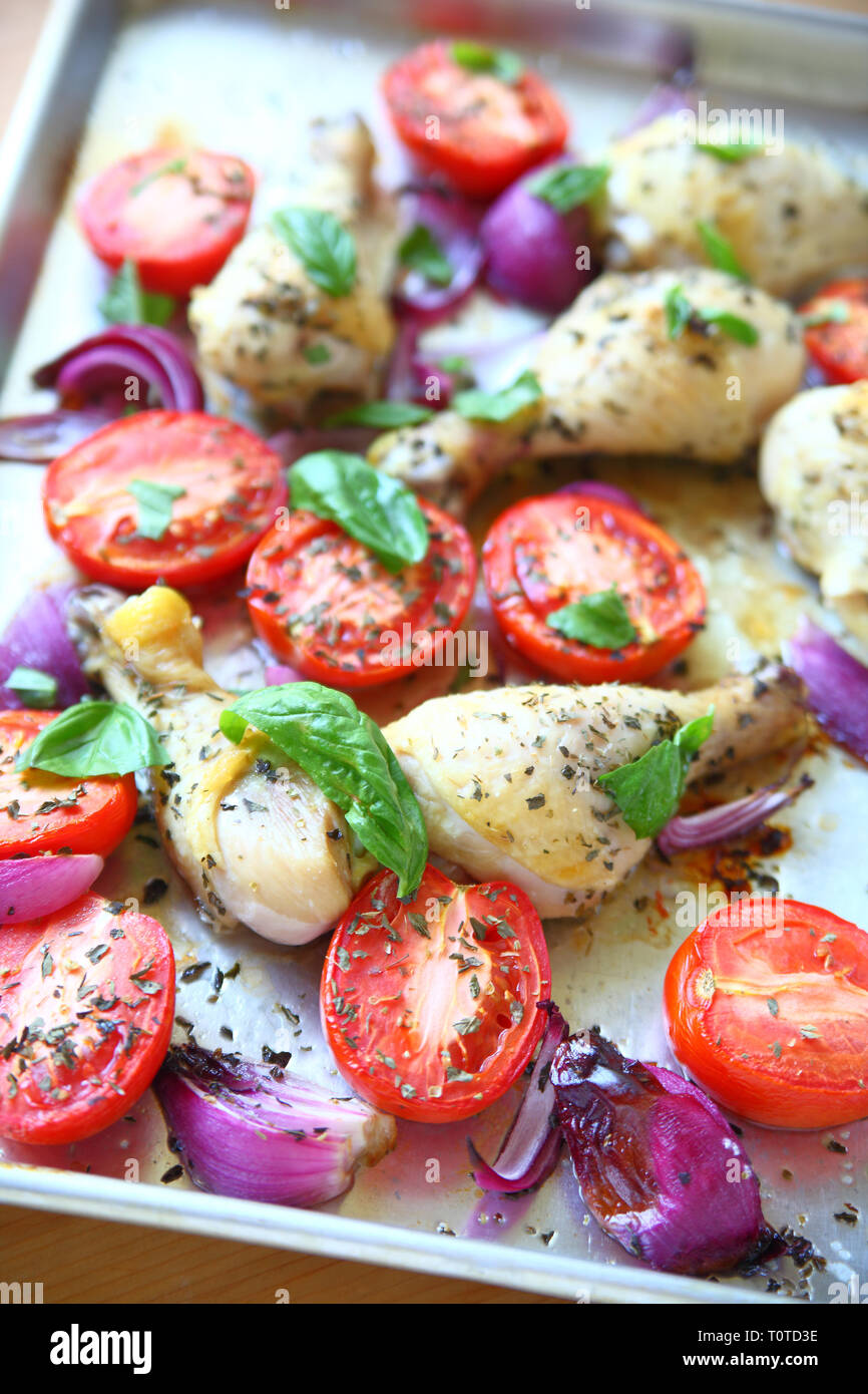 Chicken legs roasted with Roma tomatoes and red onions garnished with fresh basil leaves Stock Photo