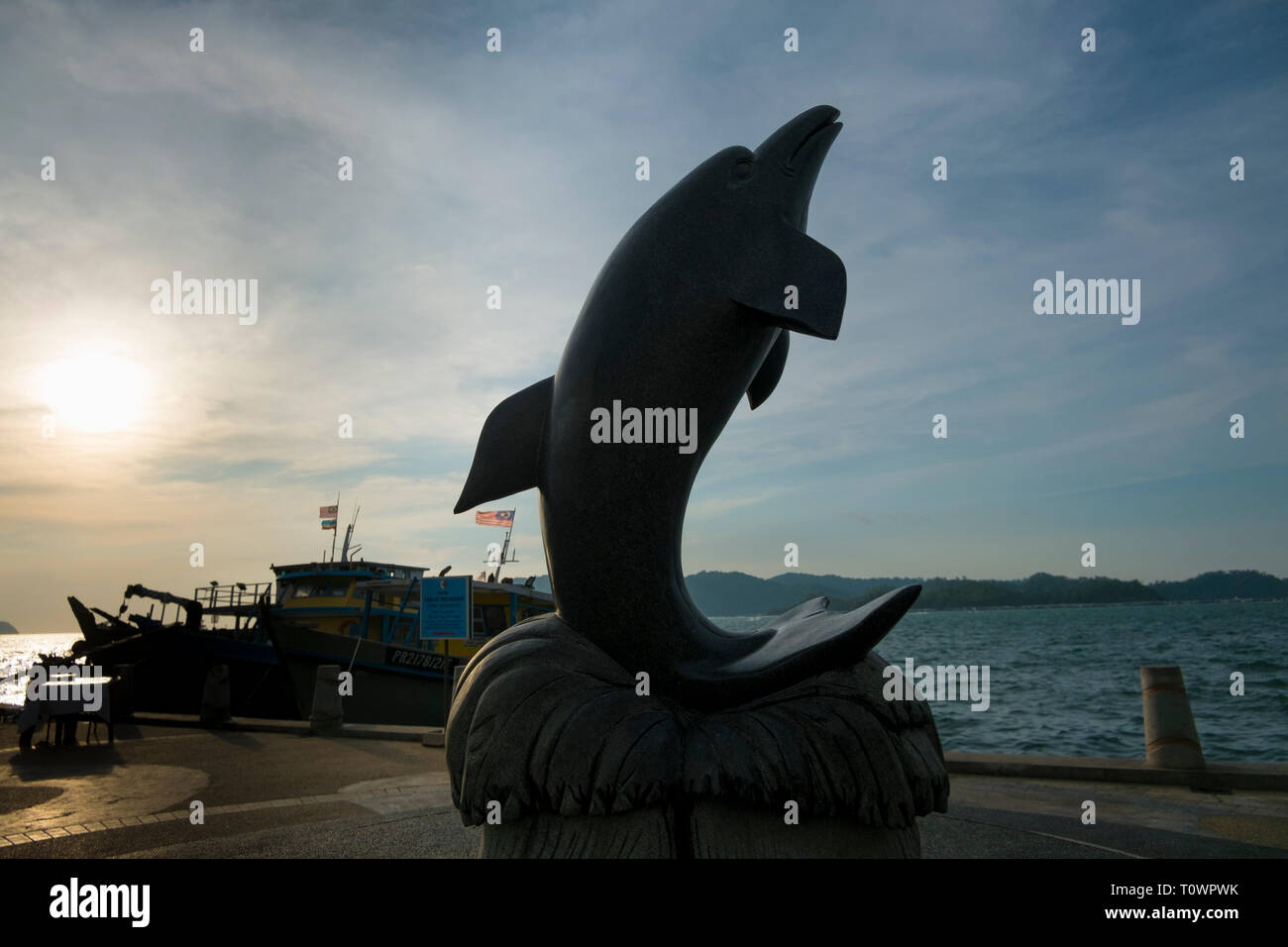 A stone dolphin sculpture is placed on the waterside promenade in Kota
