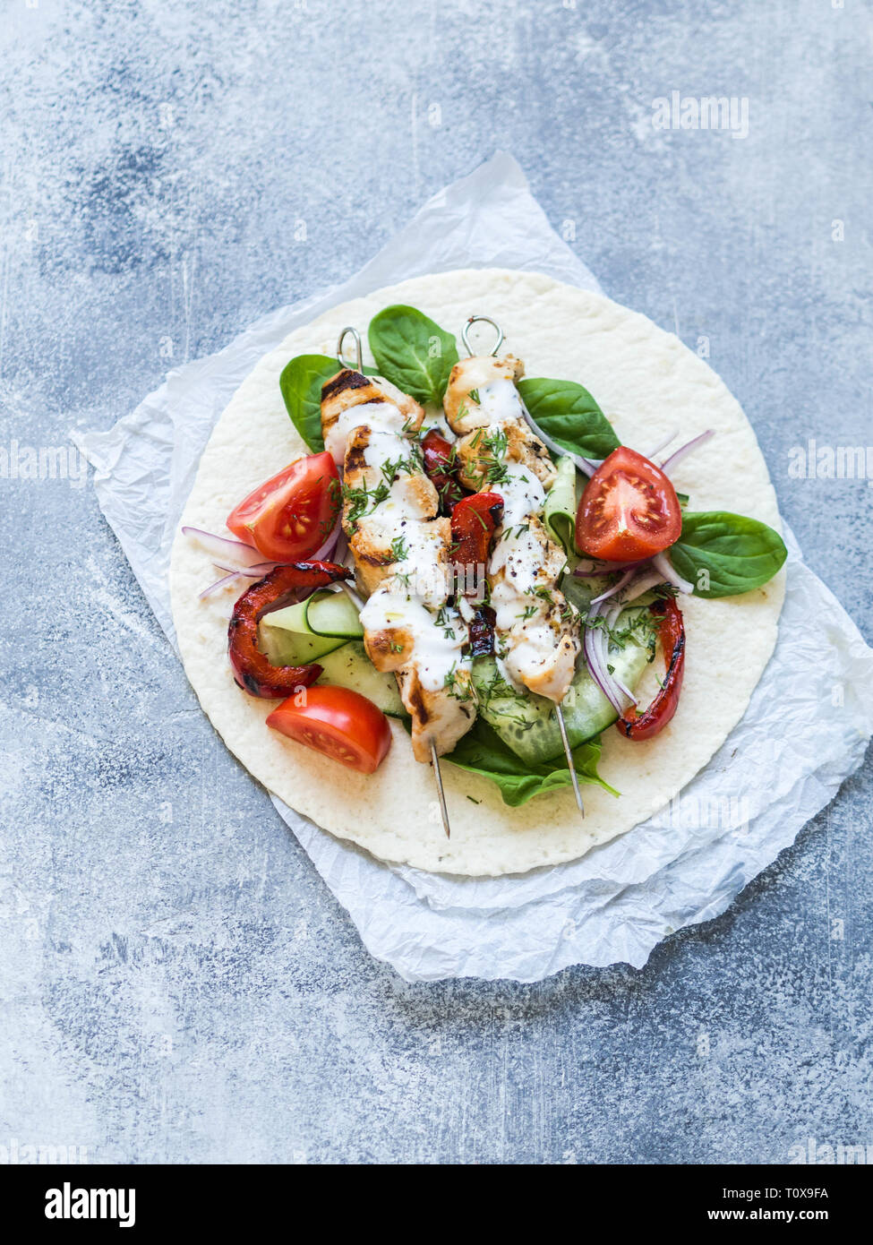 Grilled chicken on metal skewers with Greek sauce and fresh vegetables on the pita. Greek cuisine. Stock Photo