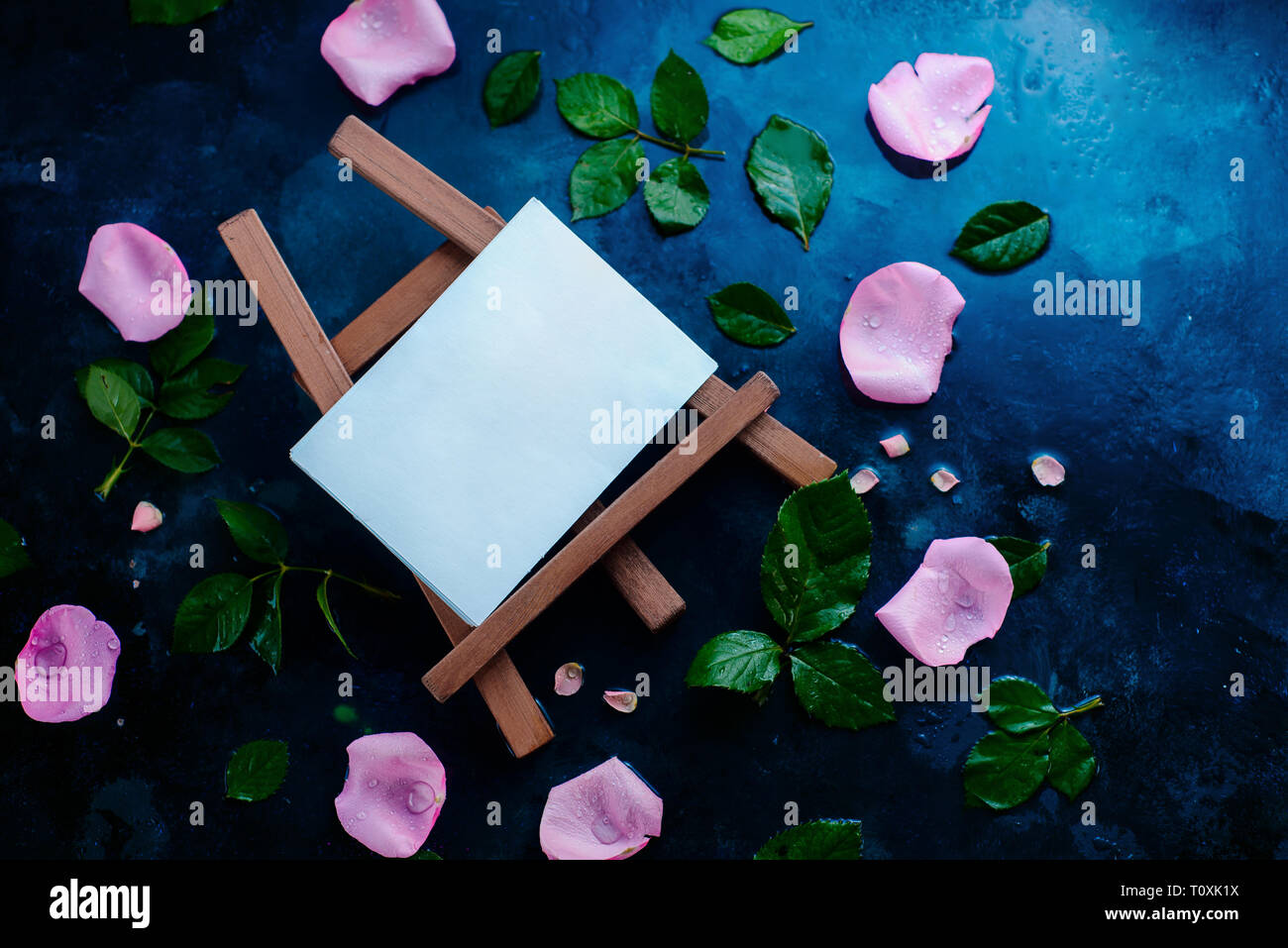 Artist easel with rose petals and leaves on a wet background with copy space. Blank template for a watercolor painting Stock Photo