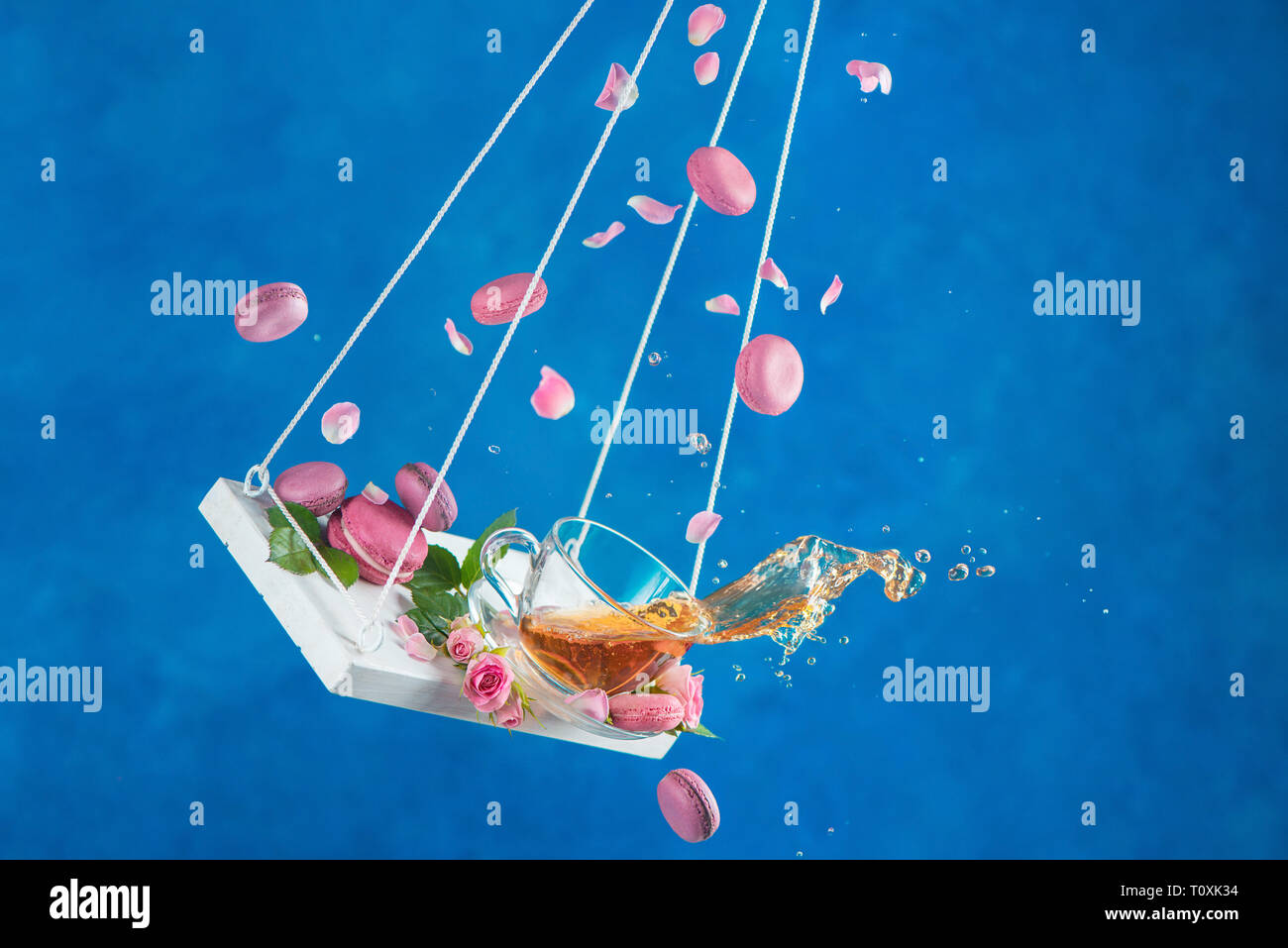 Rose tea with macaron cookies and pink flower petals on swings in motion. Action high speed photogrpahy with hot drinks Stock Photo