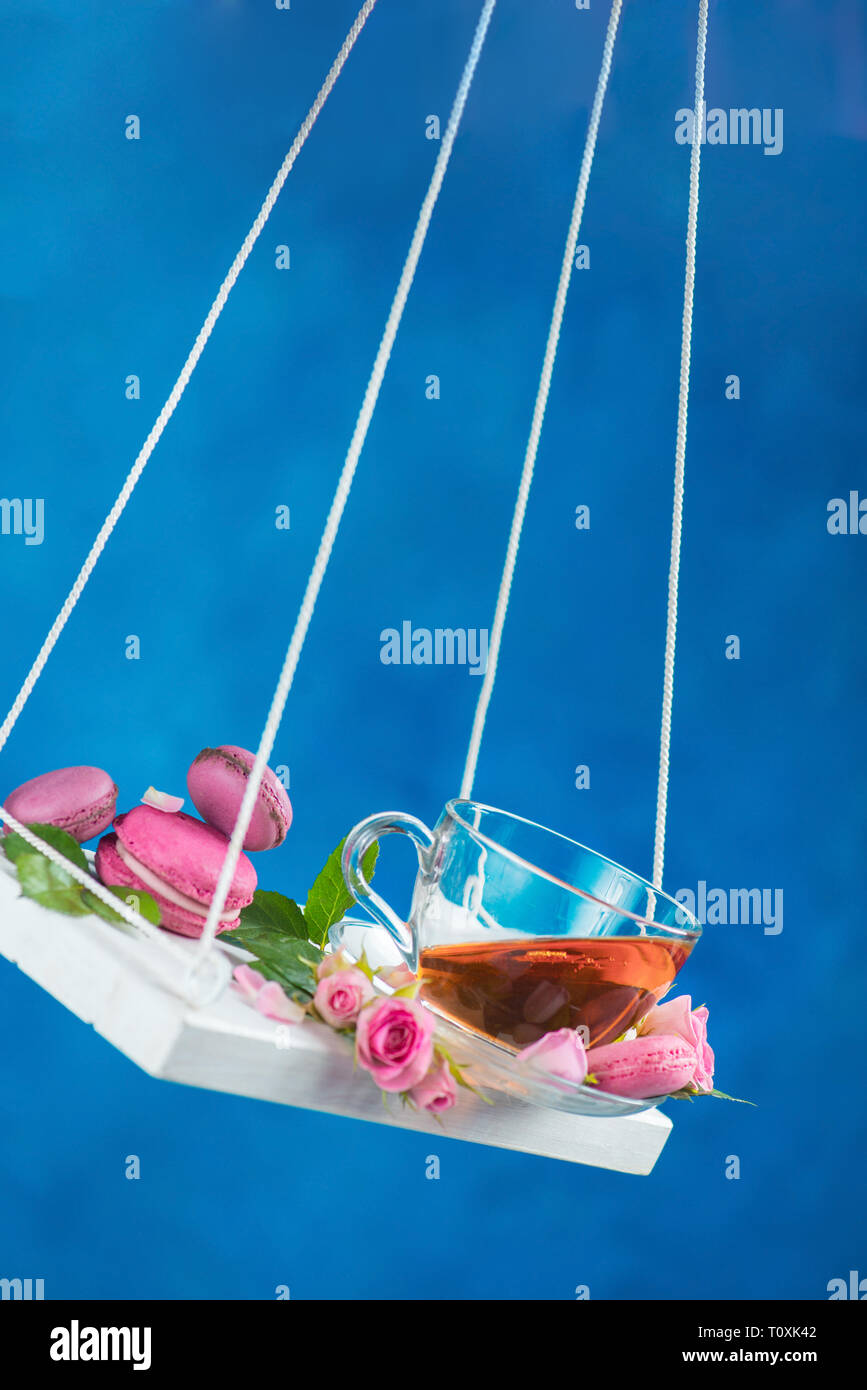 Swings in motion with rose tea, macaron cookies, and pink flowers on Spring energy concept on a vivid blue background Stock Photo
