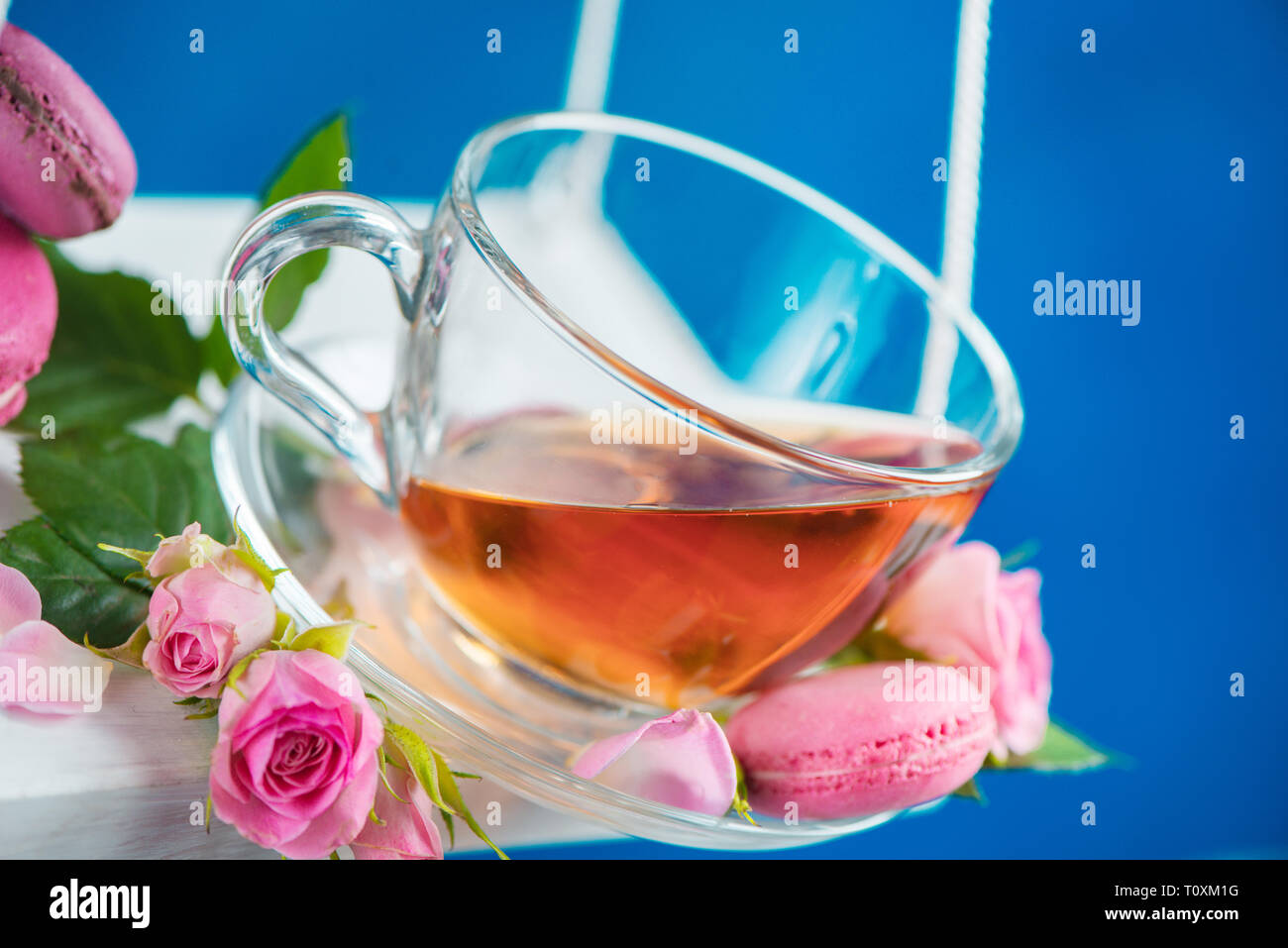 Rose tea with macaron cookies and pink flowers on swings in motion. Spring energy concept on a vivid blue background Stock Photo