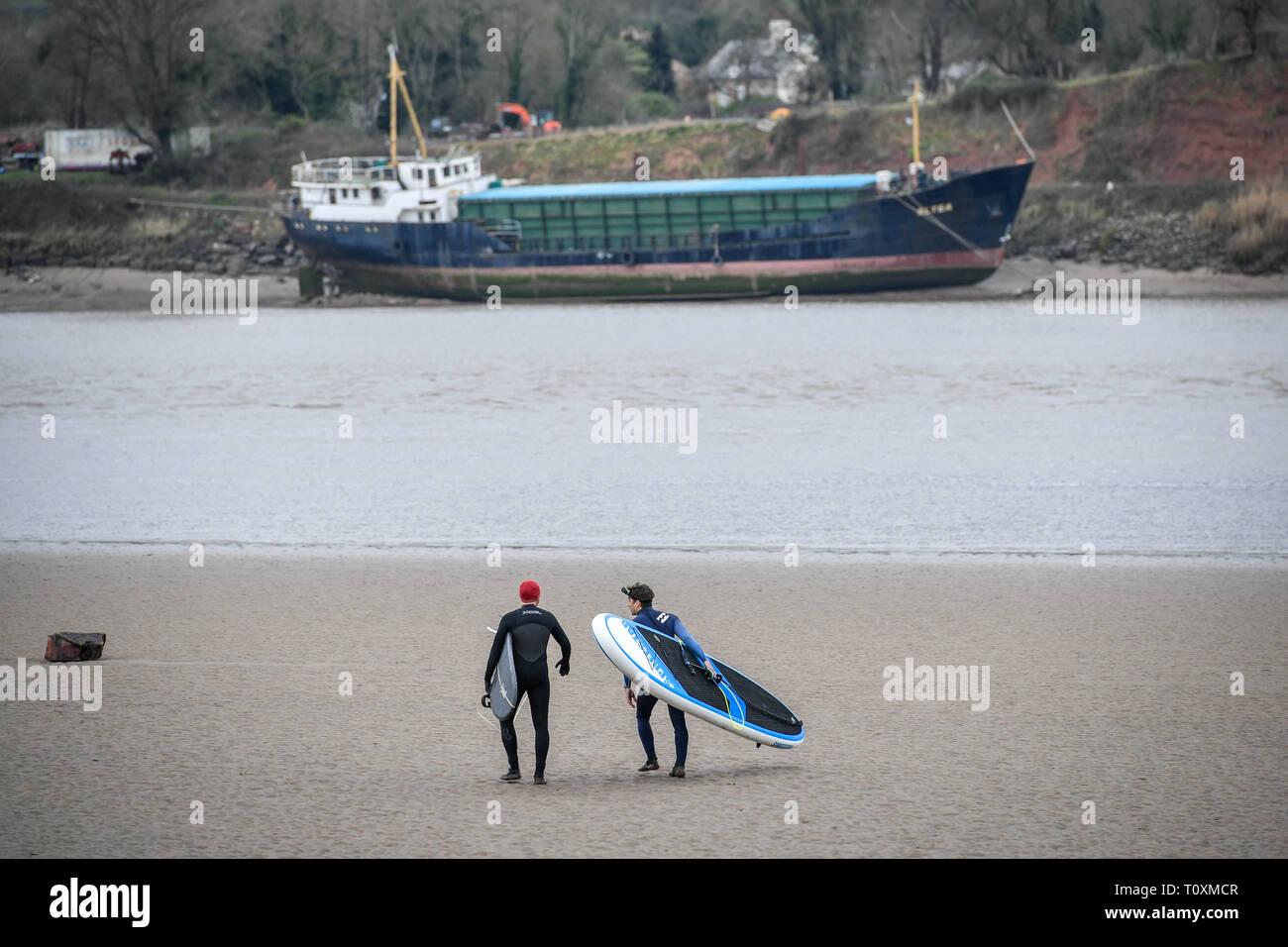 Surfers carry their boards along a sandbank as they prepare to ride the first five-star Severn Bore of 2019 at Newnham, Gloucestershire. Stock Photo