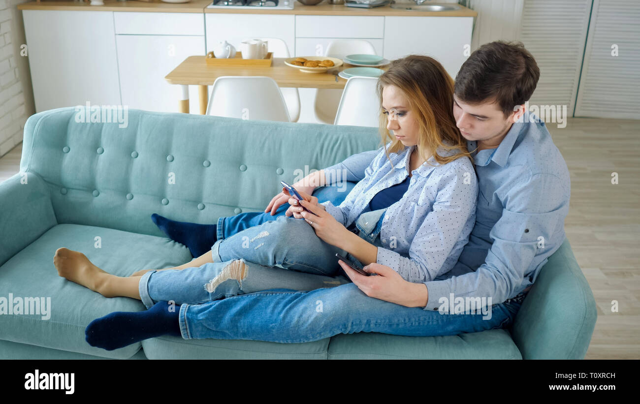 Kiwi uitdrukking klasse guy and girl sit on sofa surfing internet in smartphones Stock Photo - Alamy