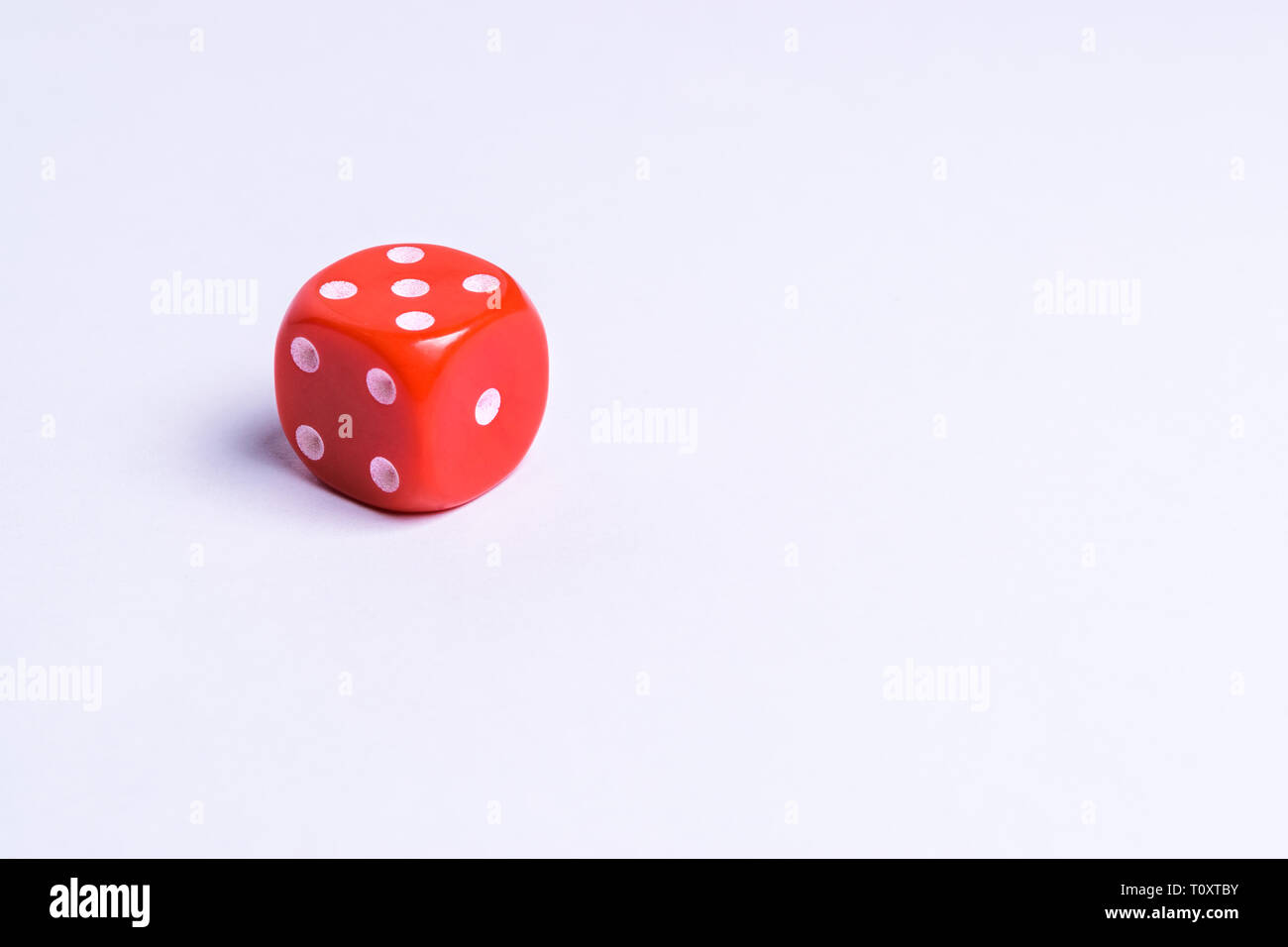 A red colored playing dice isolated on a uniform background Stock Photo