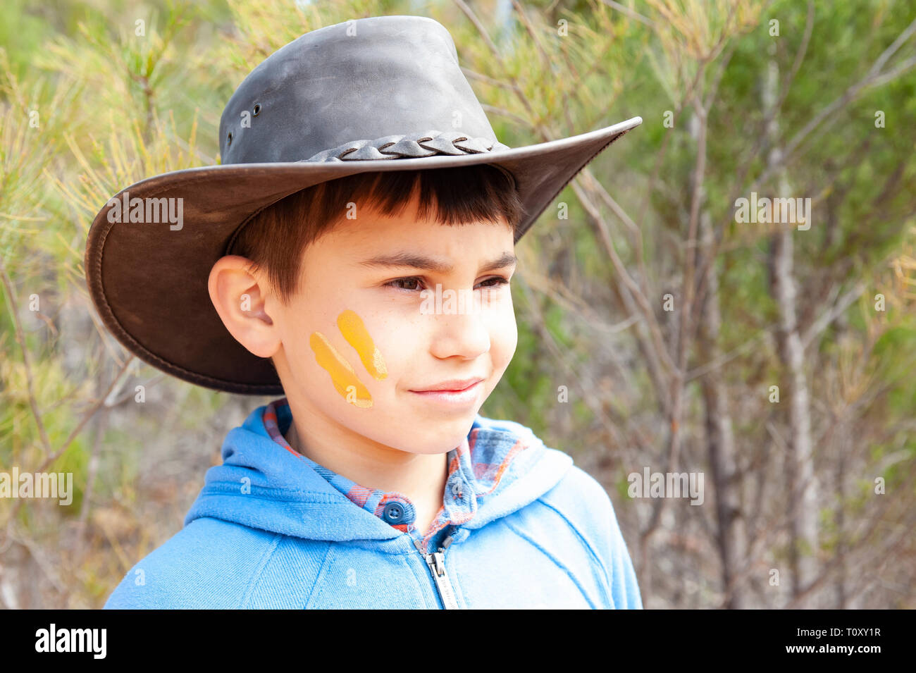 young boy in cowboy hat in the Australian bush, with yellow ochre paint