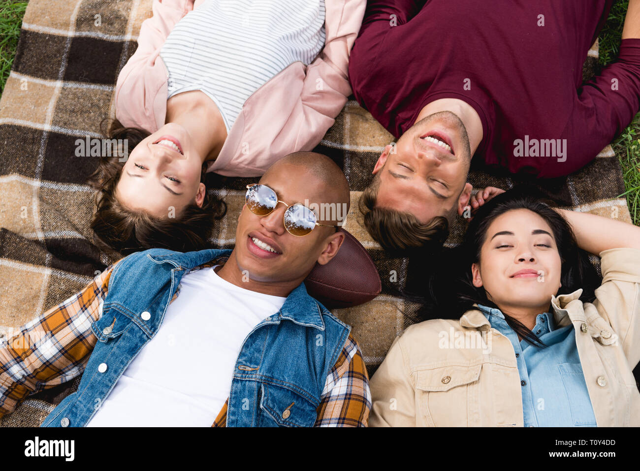 overhead view of happy multicultural friends lying on checkered blanket ...