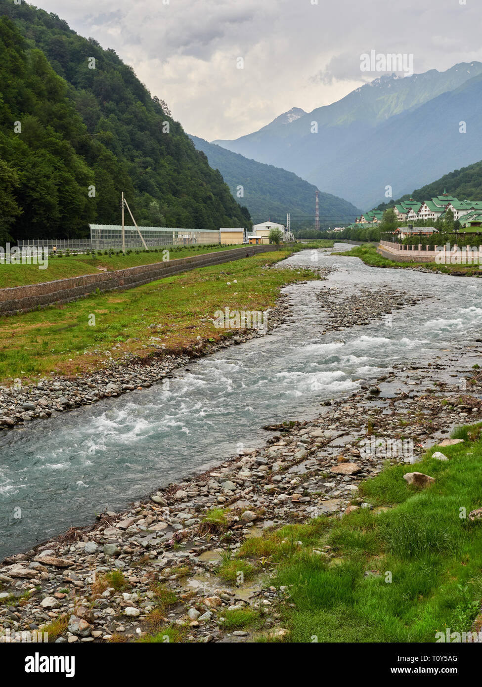 The River Flows Between The Green Mountains In Front Of The Complex Of Hotels High Mountains With Snowy Peaks In The Distance Stock Photo Alamy