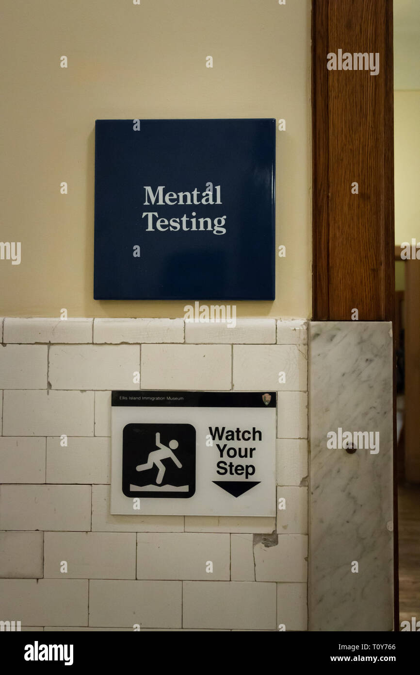 A sign on Ellis Island shows the way to the room for Mental Testing and funnily below it is a sign saying Watch Your Step. Stock Photo