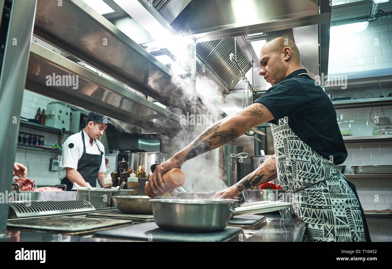 How to cook a meat Concentrated young chef in apron and cooks preparing food together in a restaurant kitchen. Cooking process Stock Photo