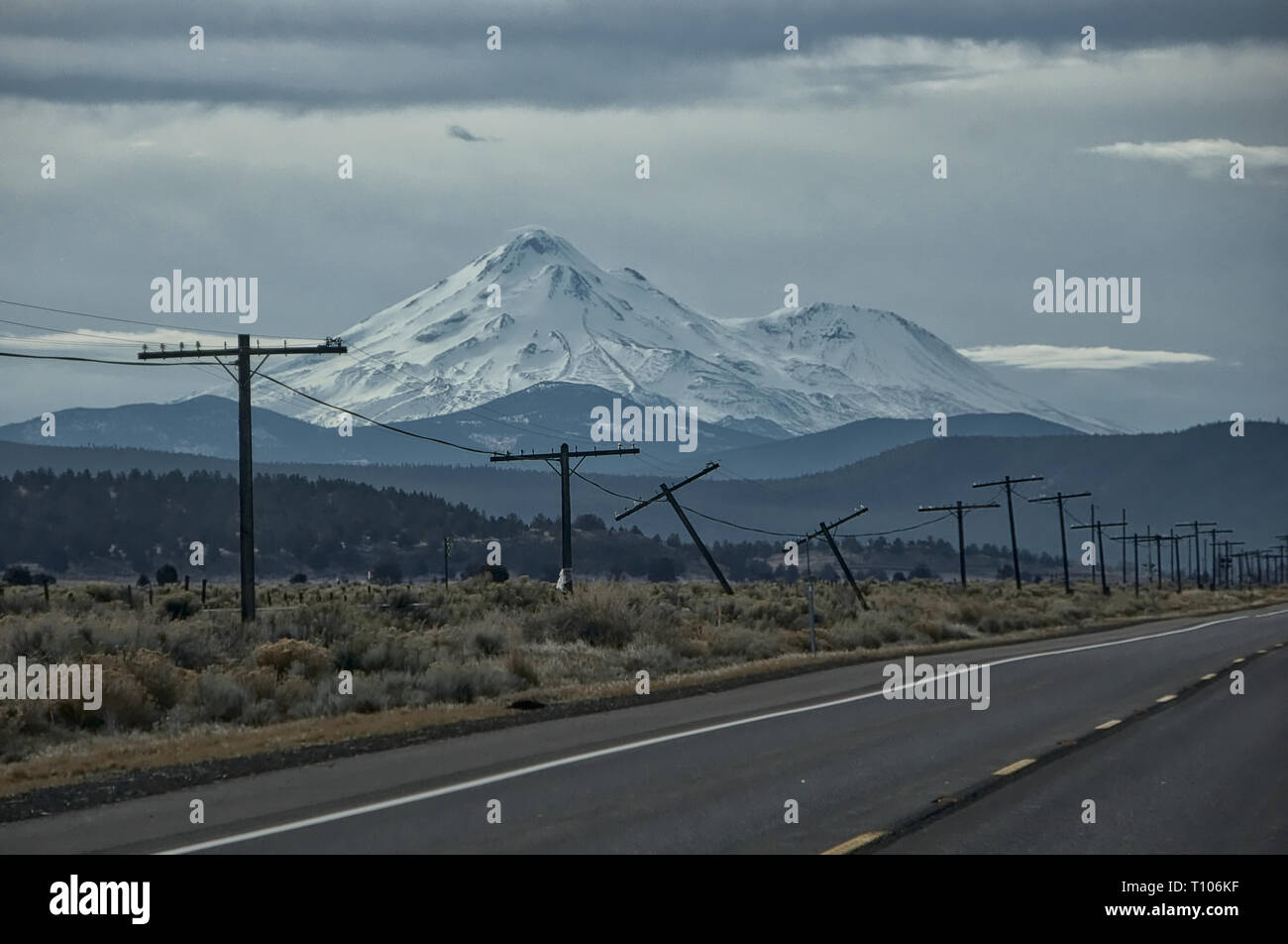 Remote Northern Californian road with the peaks of Mt. Shasta in the background and old telephone lines falling over in the foreground. Stock Photo