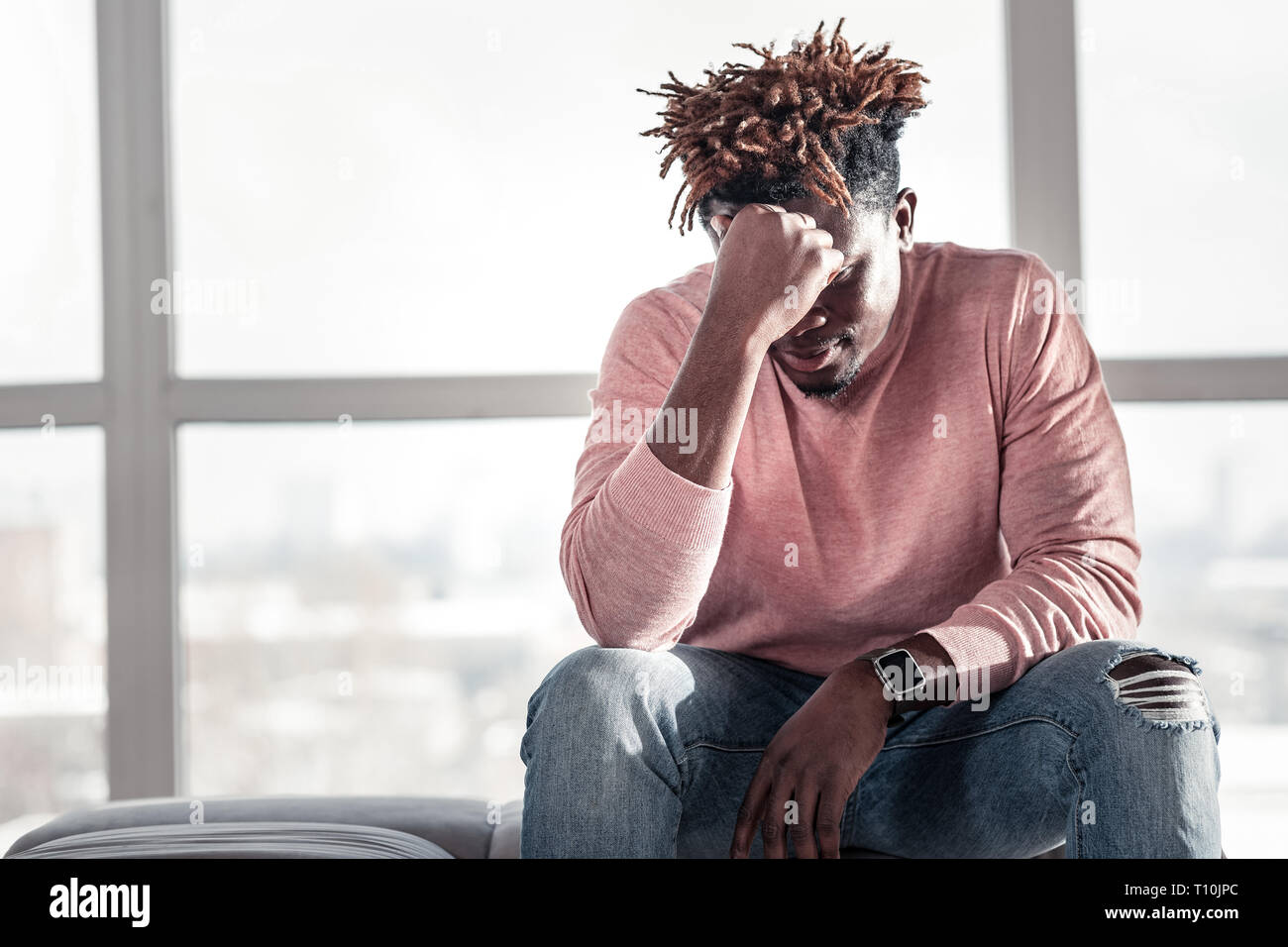 Thoughtful dark-skinned man sitting on cozy sofa Stock Photo