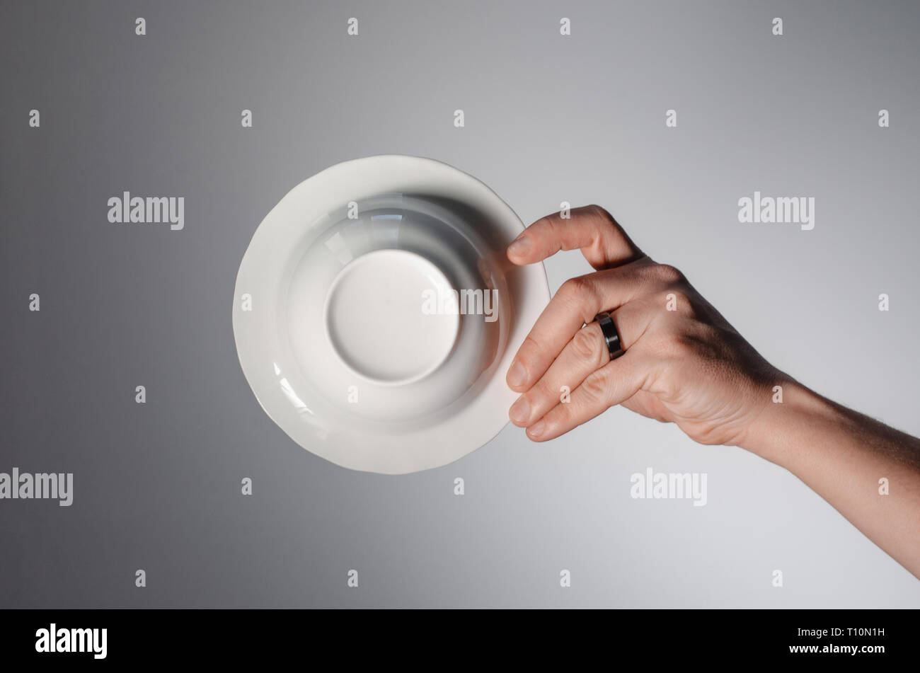 Male hand holding a white plate, on a light background. bottom view Stock Photo