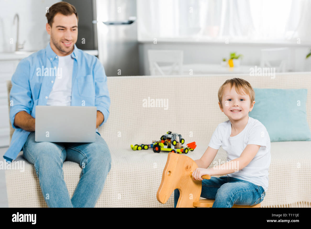 Happy Preschooler Son Riding Wooden Rocking Horse While Father