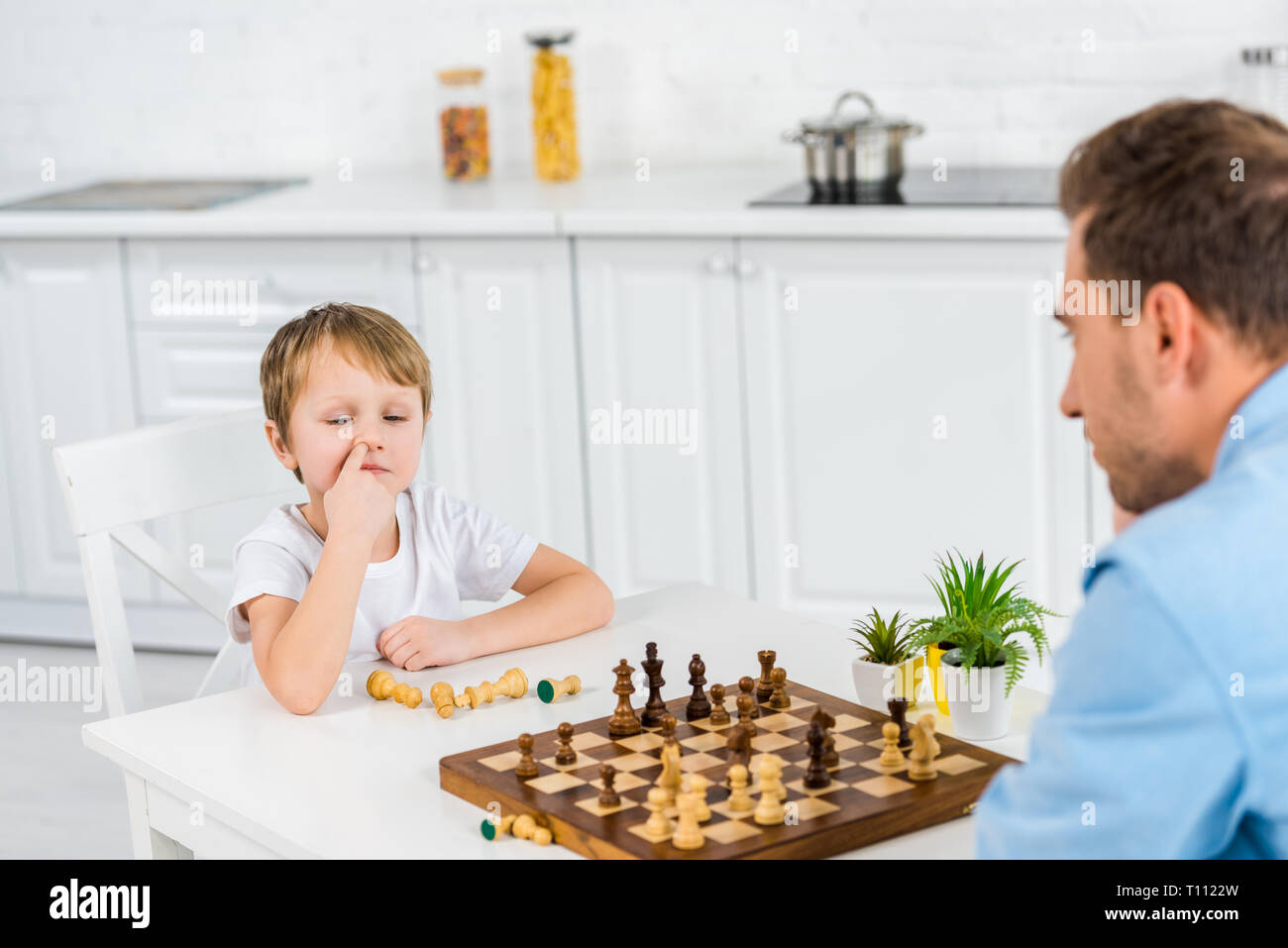 preschooler son picking nose while playing chess with father at home Stock Photo