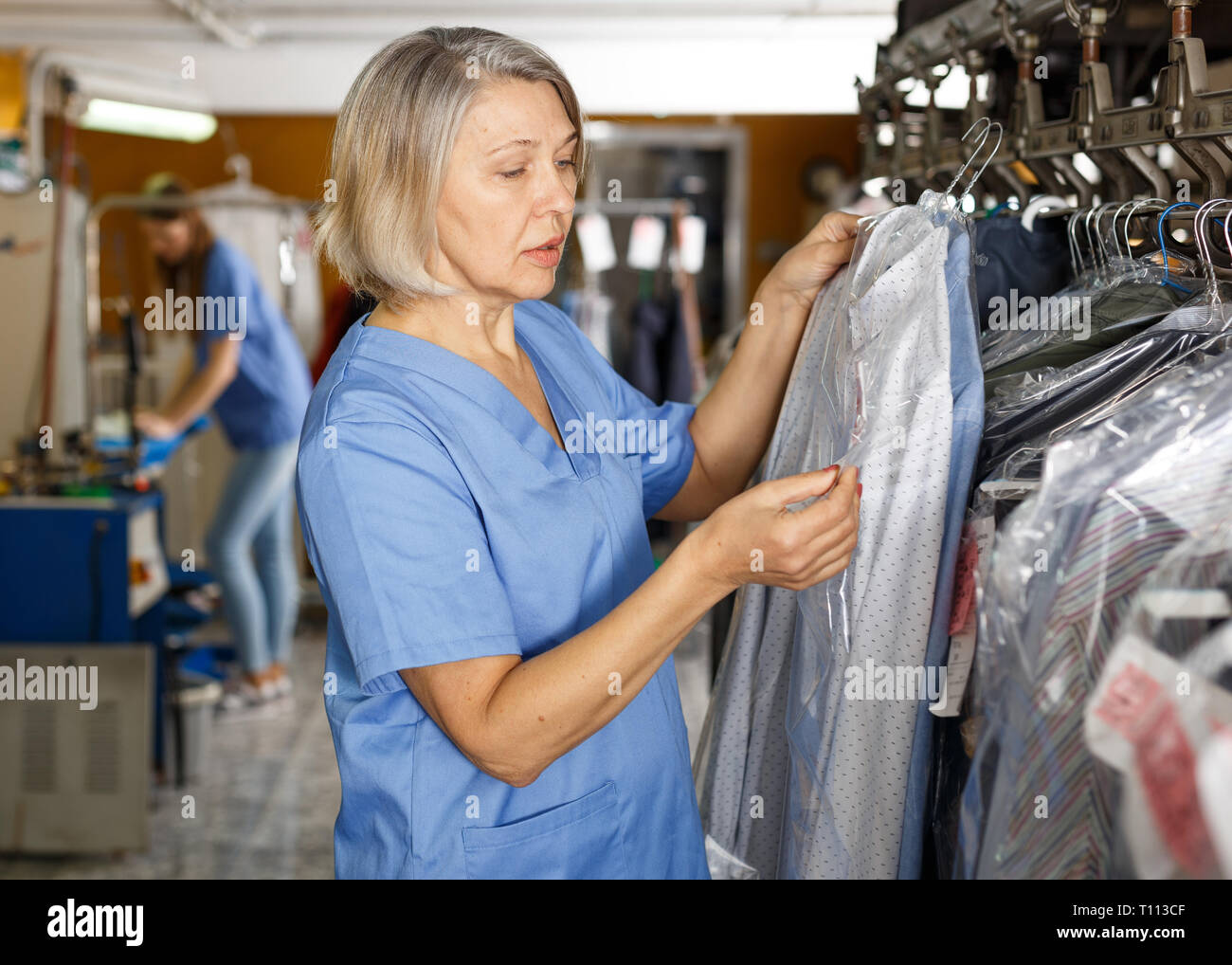 Portrait of friendly female dry-cleaning salon worker among racks with clean clothes Stock Photo