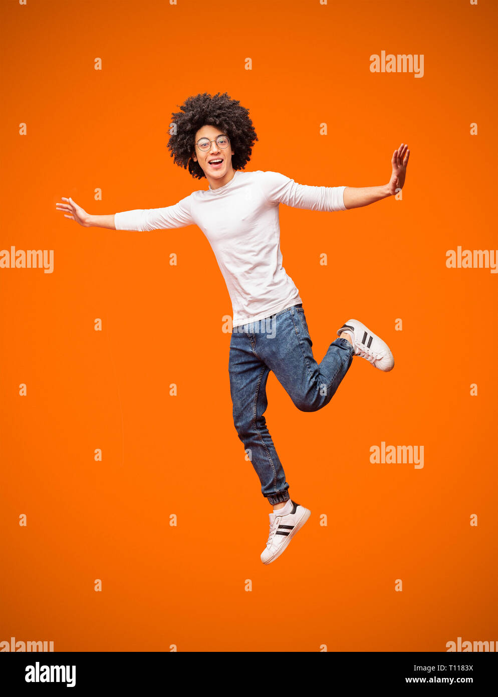 Happy black guy jumping on orange studio background Stock Photo