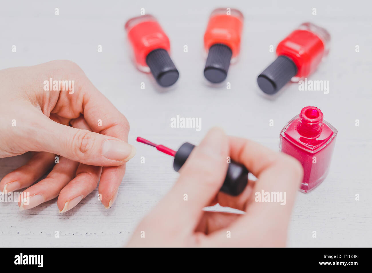 woman's hands with red nail polish bottle and other colors on wooden surface, concept of beauty indusry and cosmetics Stock Photo