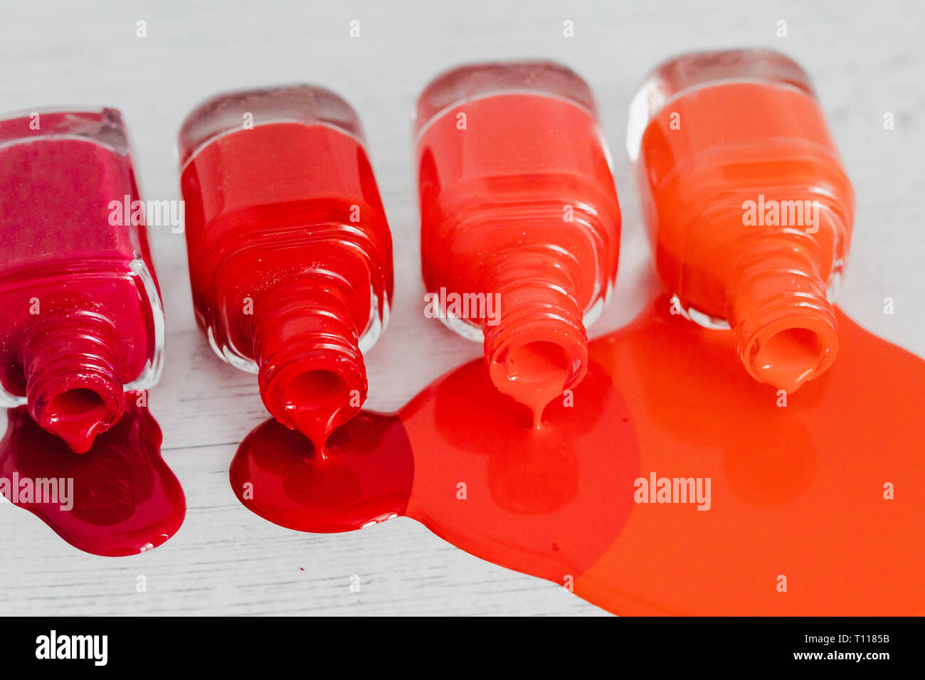 nail polish bottles in different shades of red to orange and purple spilling color on wooden surface, concept of cosmetics industry and manicure Stock Photo