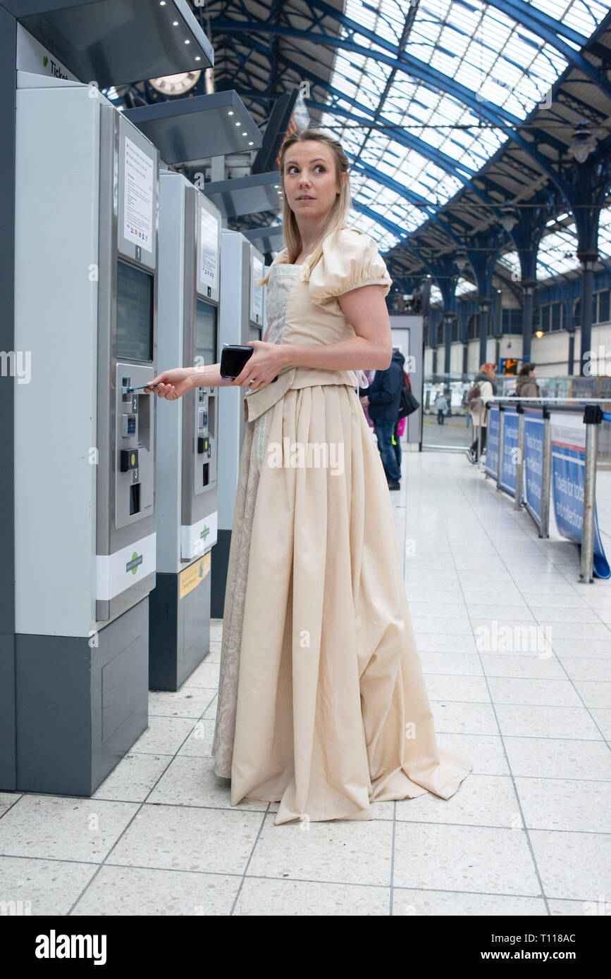 a young white woman collects her train ticket from a ticket machine at ...