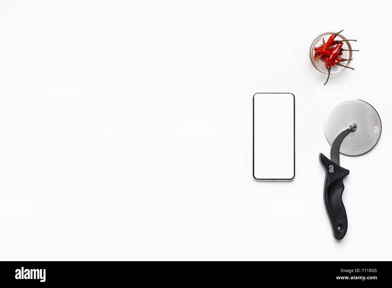 Phone with blank screen, cutter and bowl with chilli peppers Stock Photo