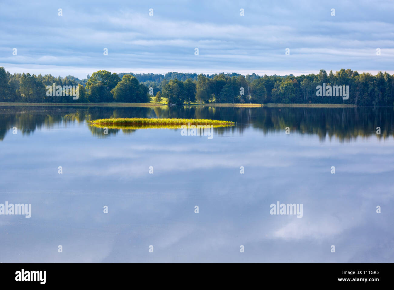 Blue sky, clouds and green trees on the banks are reflected in the quiet calm water of a lake in summer sunny day Stock Photo