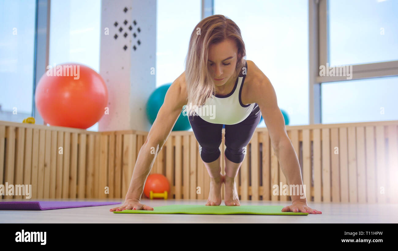 Young woman fitness trainer doing push ups in the bright studio Stock Photo