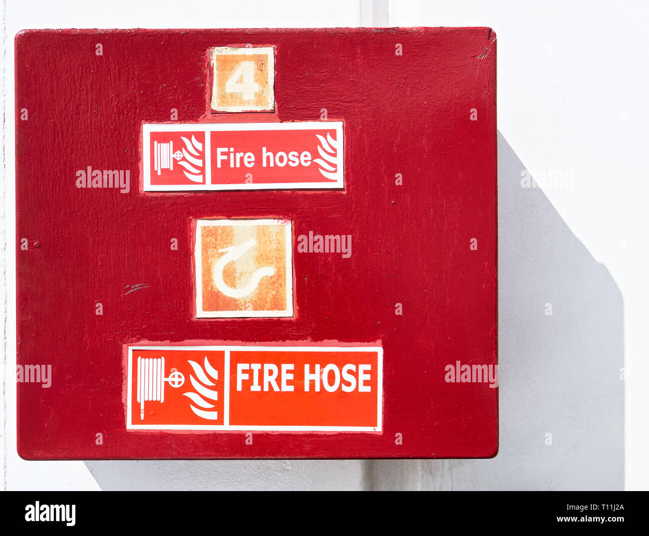 Close-up of closed red colored repainted fire hose cabinet box in front of a white wall, seen on a ship in the Philippines Stock Photo