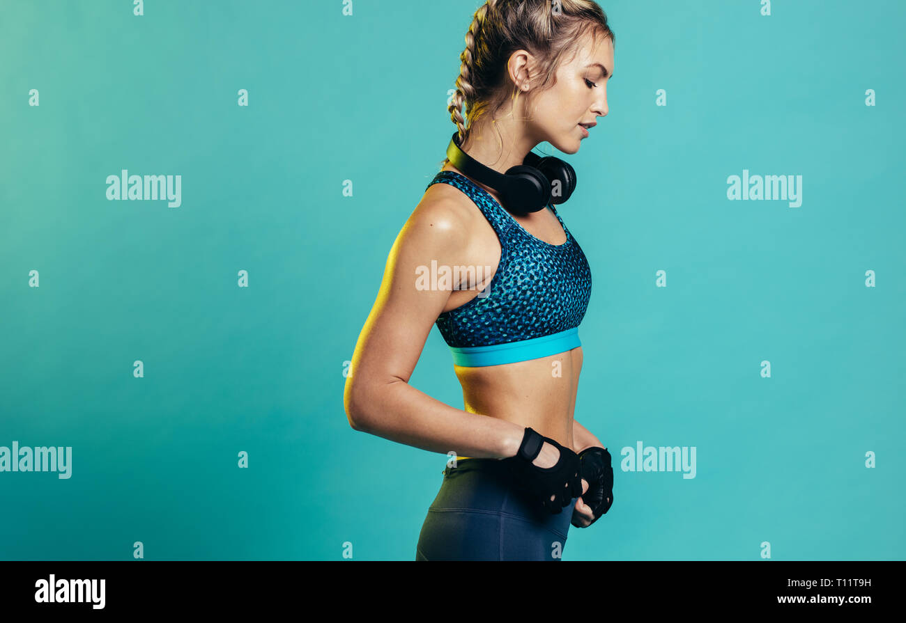 Strong fitness woman with headphones standing on blue background. Caucasian female in sports clothing standing in studio. Stock Photo
